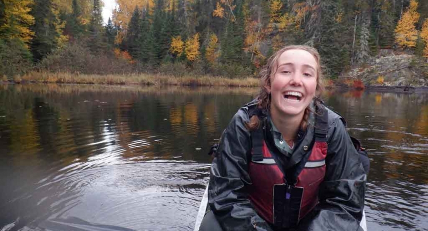 a young person wearing life jacket sits in a canoe and smiles at the camera